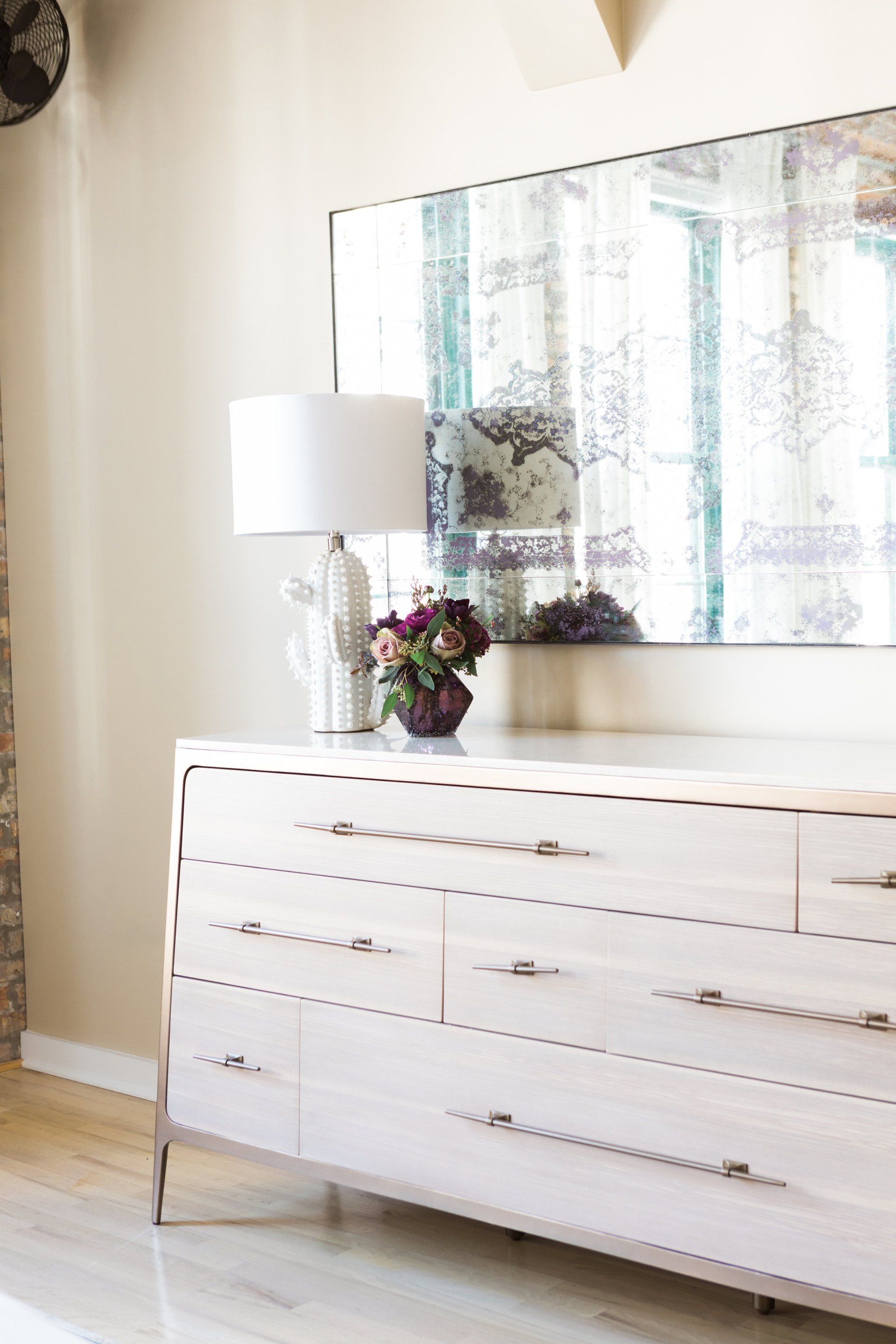 A white dresser with a mirror and a lamp on it in a room.