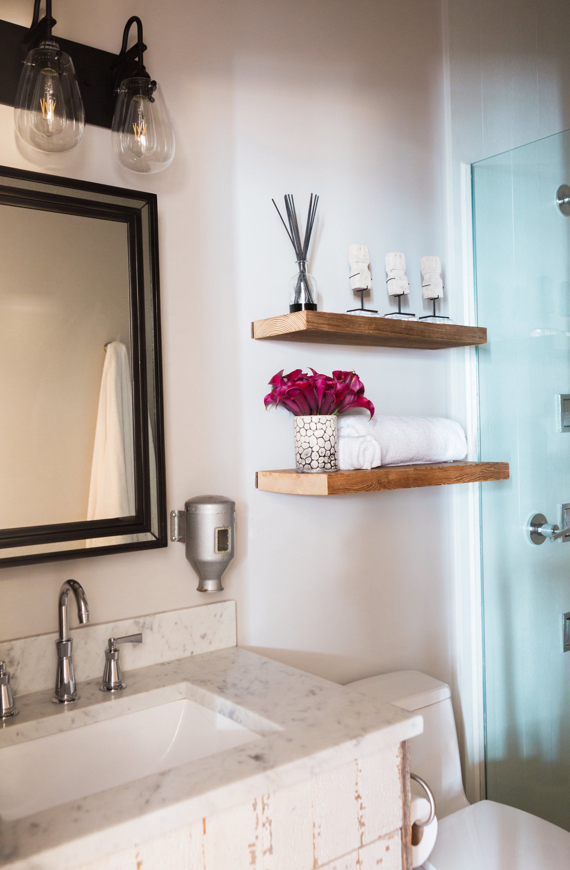 A bathroom with a sink , toilet , mirror and shelves.