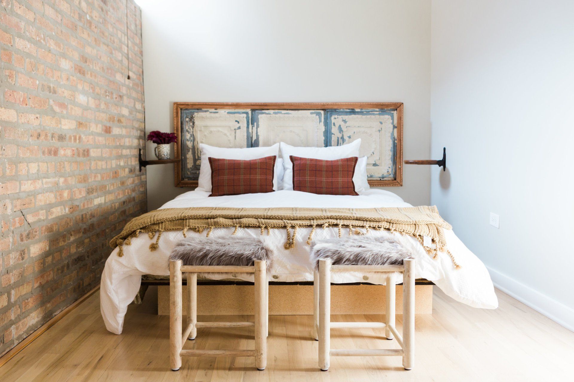 A bedroom with a bed , two benches and a brick wall.