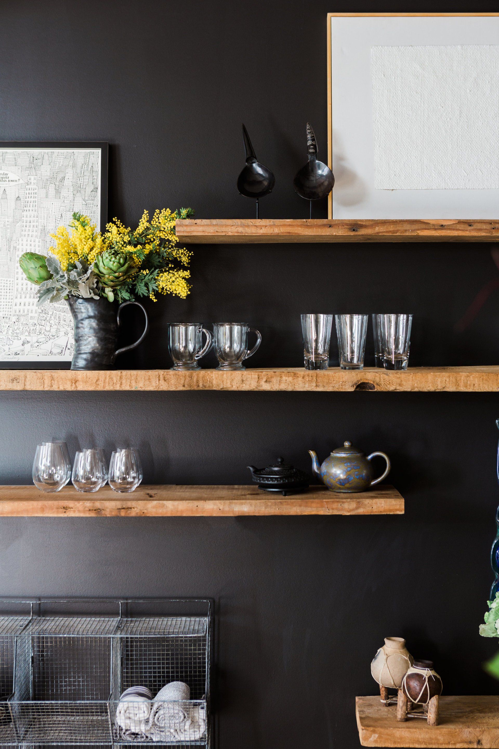 A kitchen with a black wall and wooden shelves filled with dishes and glasses.