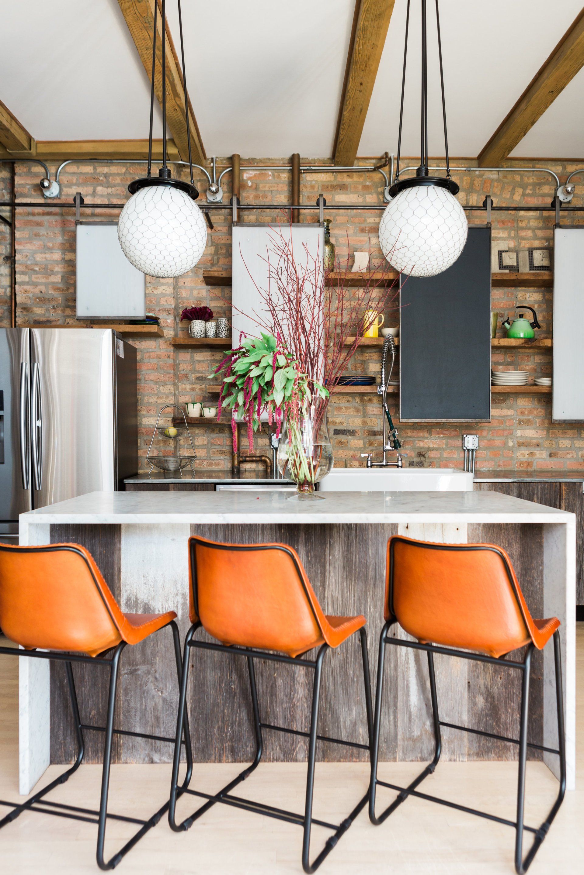 A kitchen with a large island and three orange bar stools