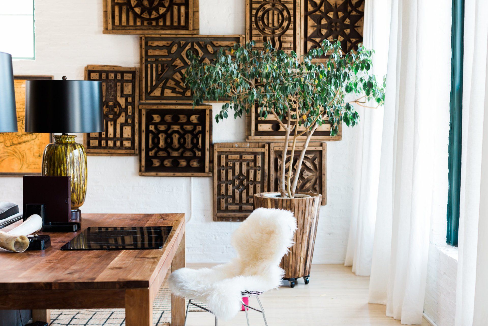A home office with a wooden desk , chair , lamps , and a potted plant.