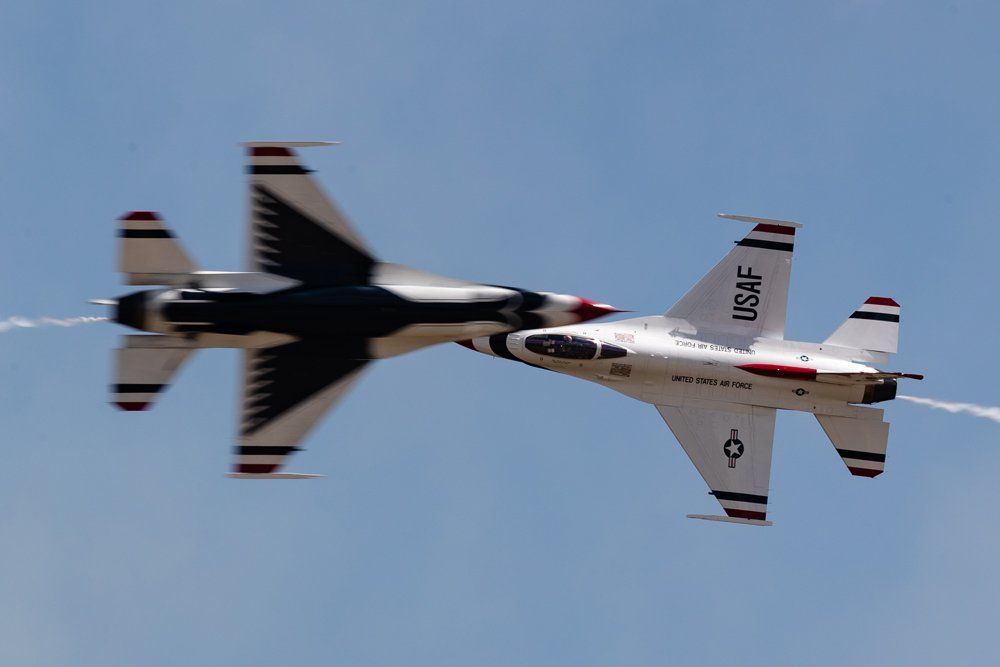 Two US Air Force Thunderbirds F-16s performing an aerial maneuver, wings close. Blue sky background.