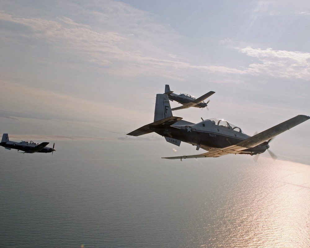 Three military propeller aircraft flying over water.