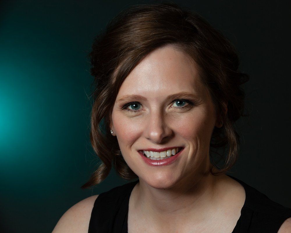 Woman with brown hair smiles, against a teal backdrop.