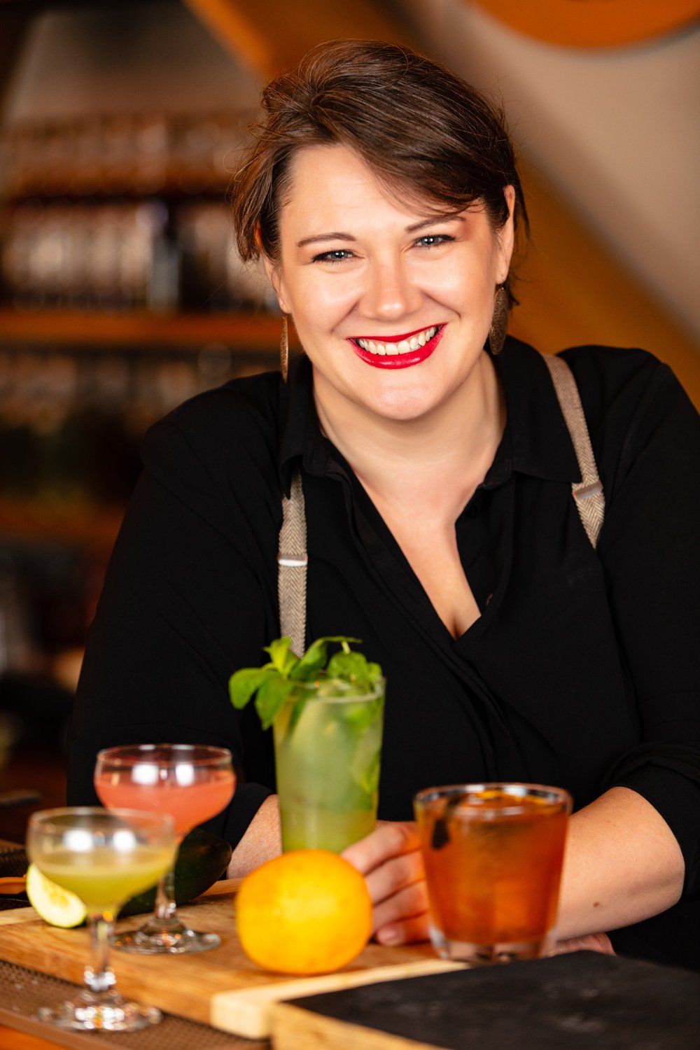 Bartender smiling, behind cocktails, wearing black shirt and suspenders.