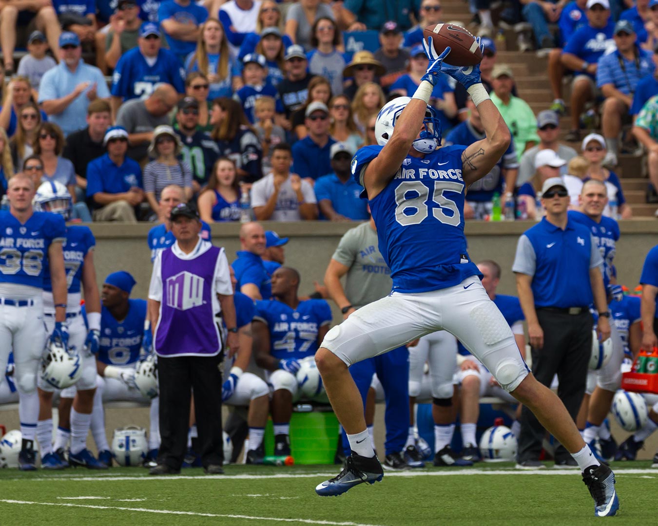 Football player in blue jersey, leaping to catch a ball, Air Force stadium.