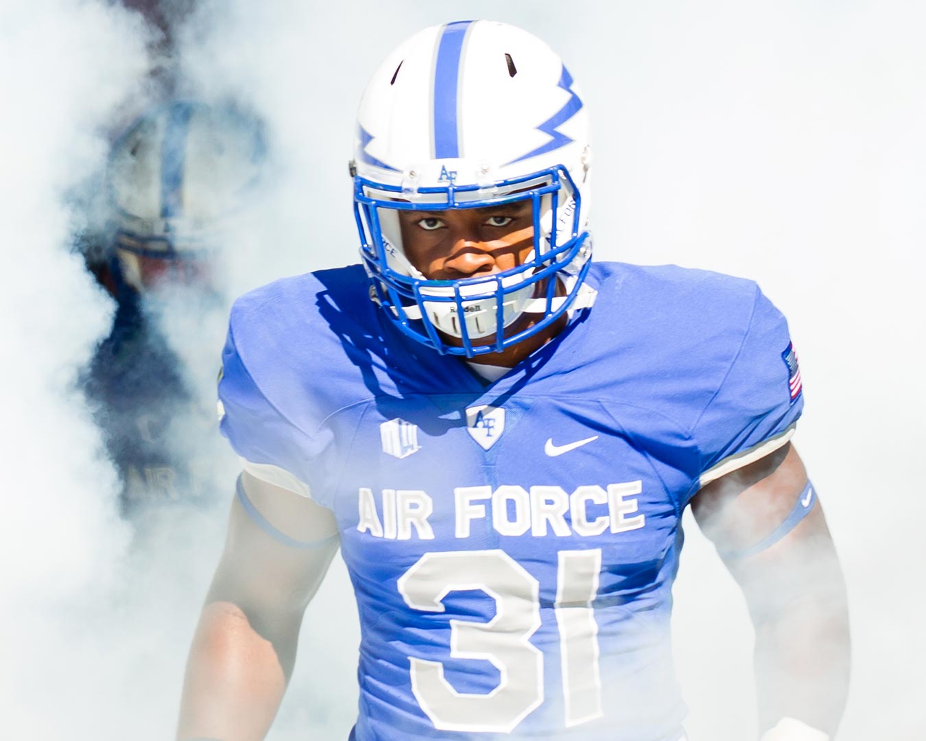 Football player in blue uniform with helmet, Air Force, emerges from smoke, number 31.