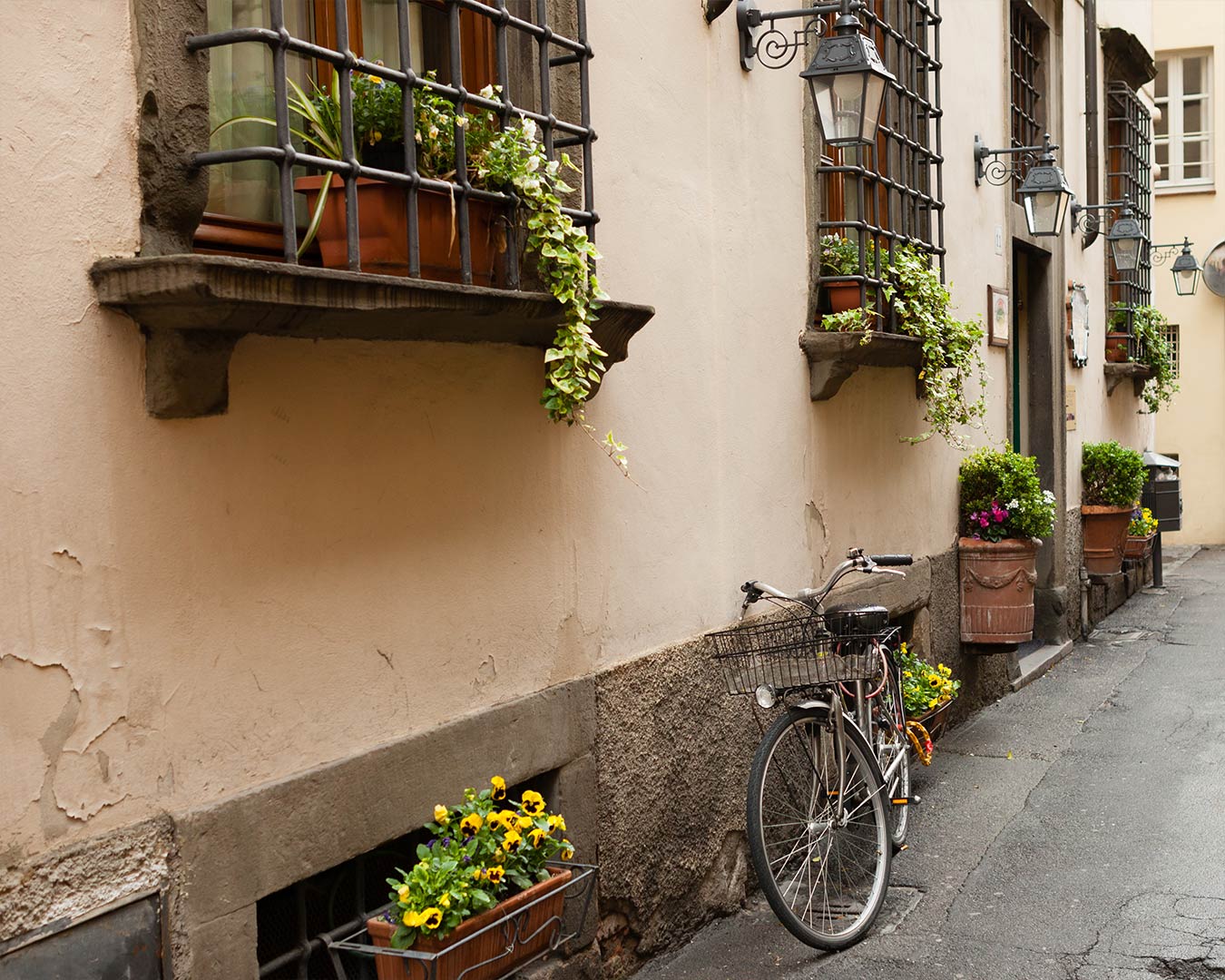 Old building facade with barred windows, flower boxes, and a bicycle on a narrow street.