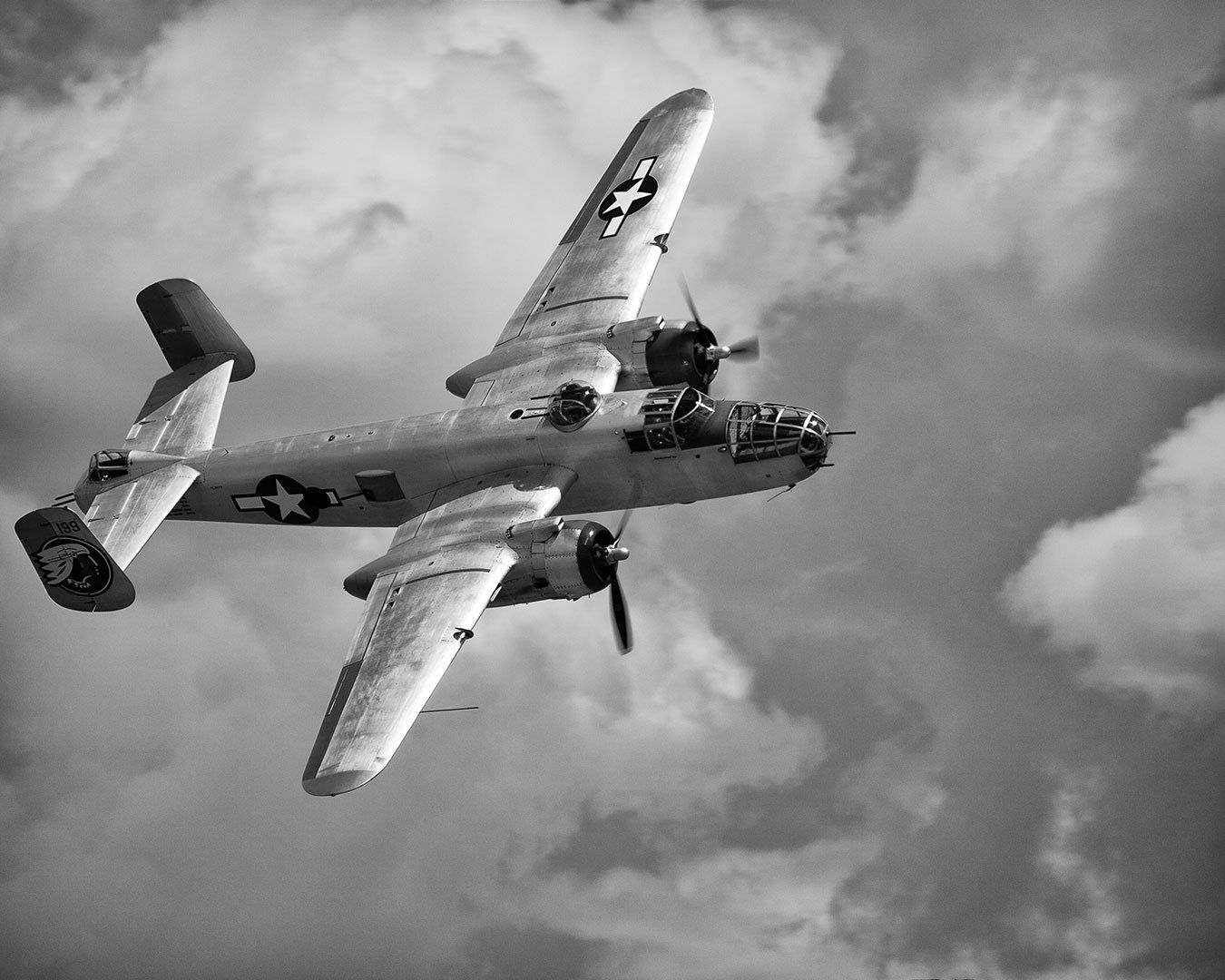 Black and white view of a twin-engine bomber aircraft in flight against a cloudy sky.