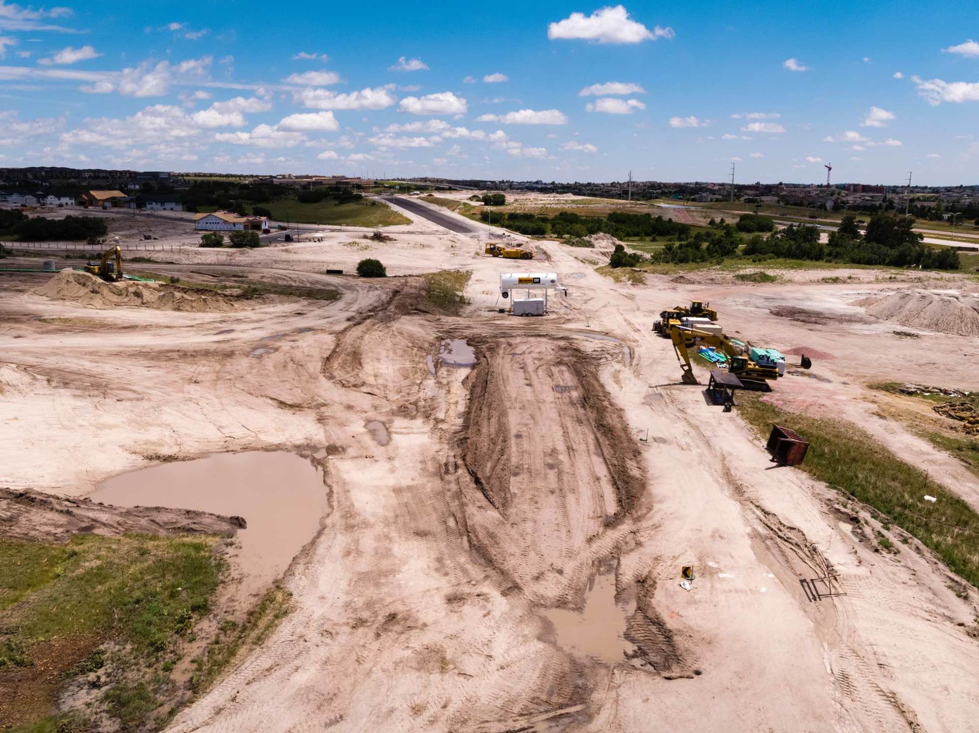 Aerial view of construction site with dirt, machinery, and a road under development under a blue sky.