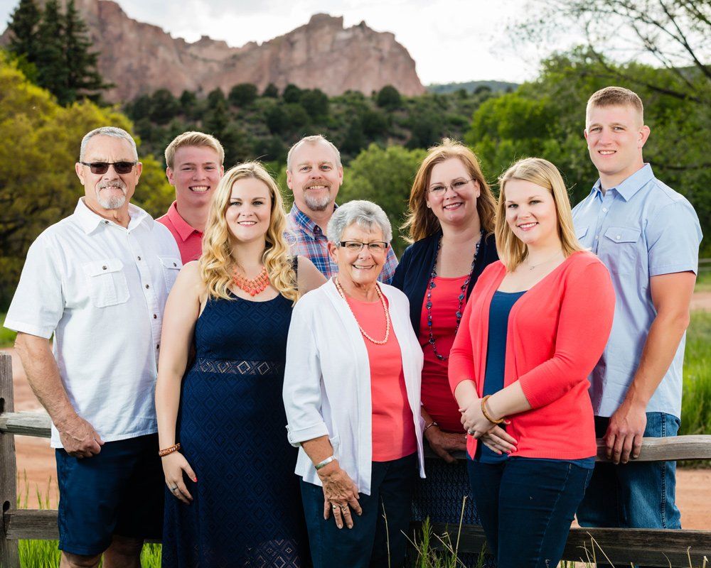 Group of people posing outdoors, smiling. Mountains and foliage in the background. Several people wearing red.