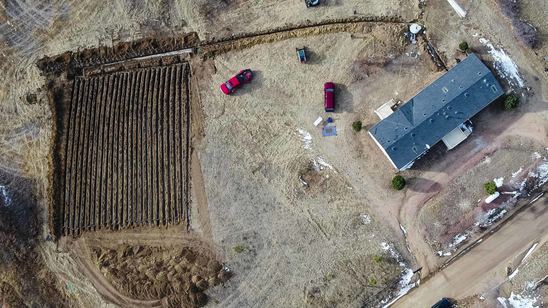 Aerial view of a home with a red car parked on the property. A large field is to the left.
