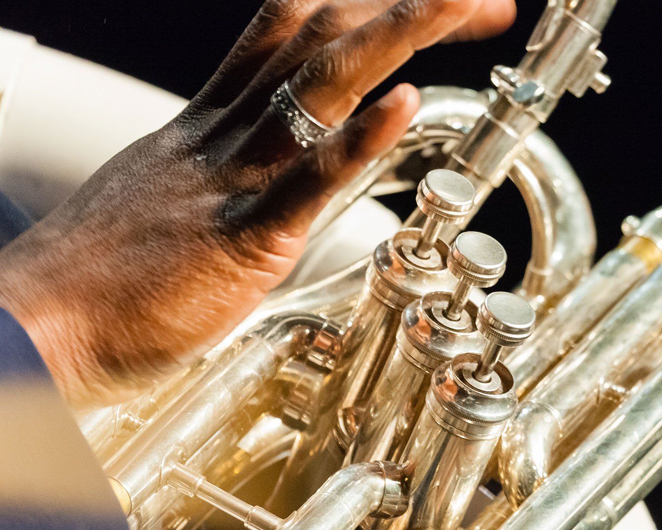 A hand with a silver ring playing a shiny brass euphonium.