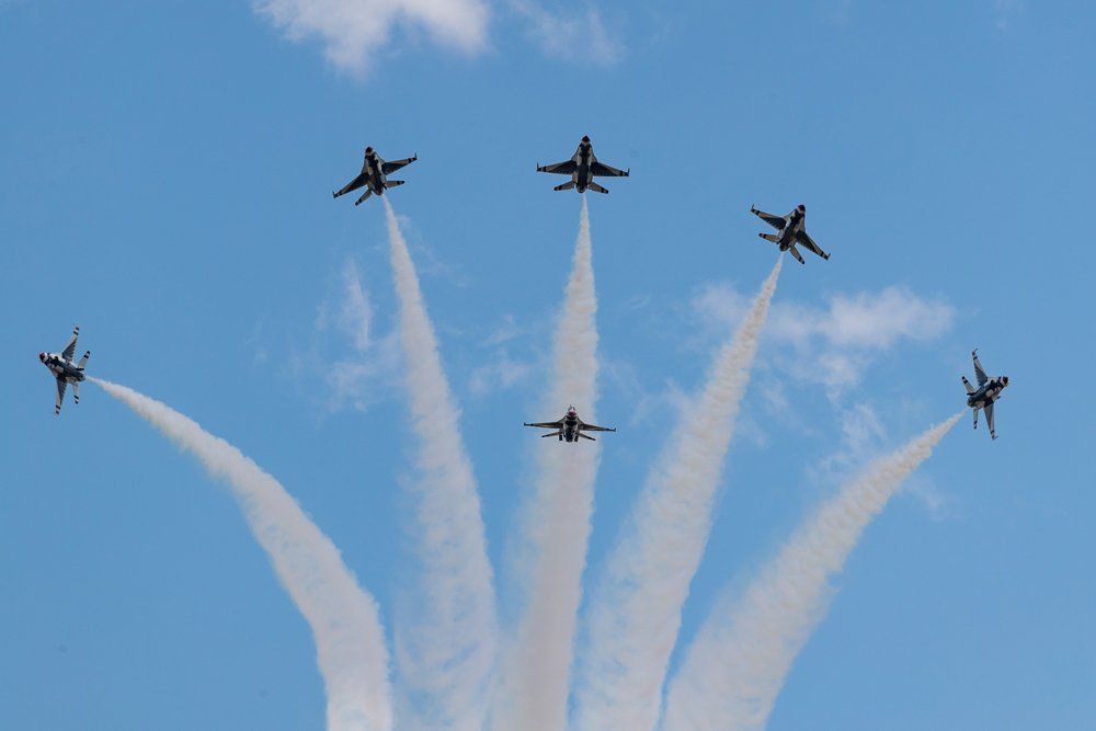 Formation of six fighter jets in the blue sky, leaving white contrails.