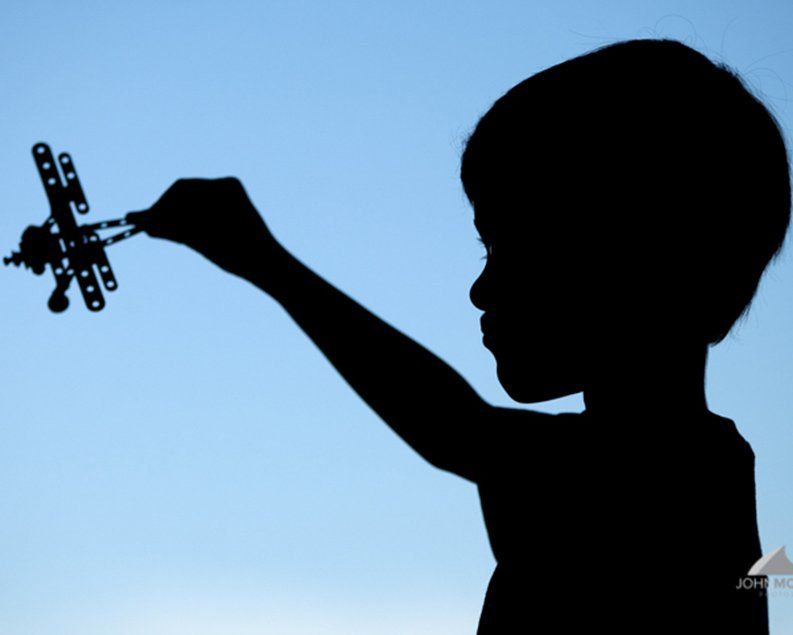 Silhouette of a child holding up a toy airplane against a blue sky.