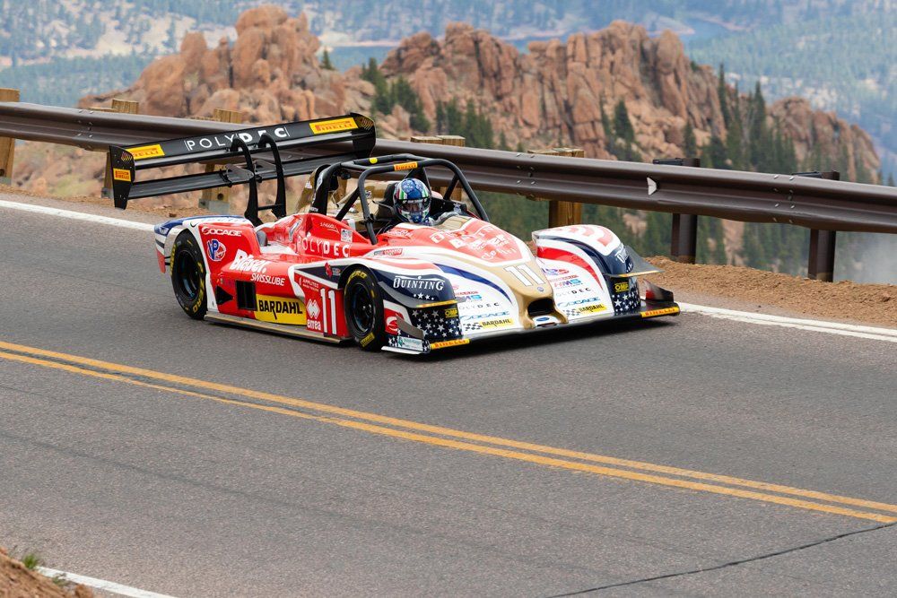 Red and white race car on a mountain road, with a mountain in the background.