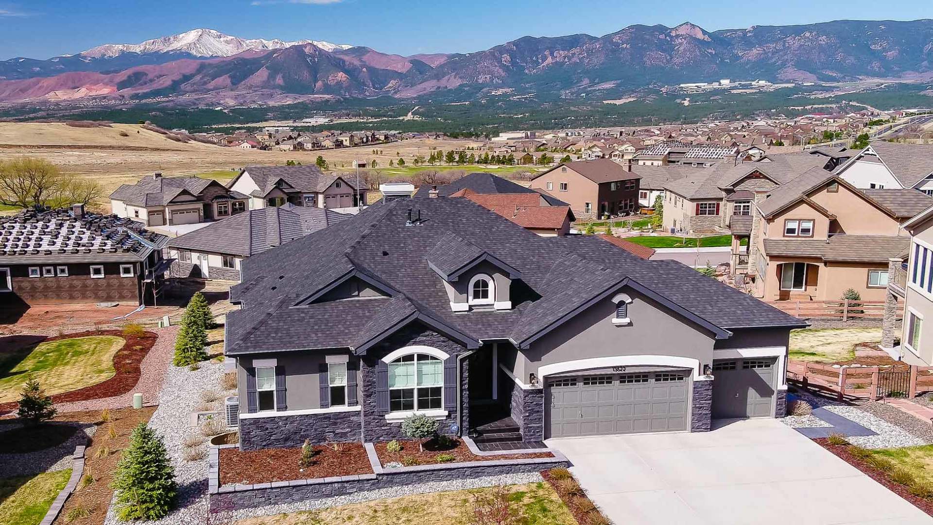 A gray house with a dark roof in a residential area, mountains in the background.