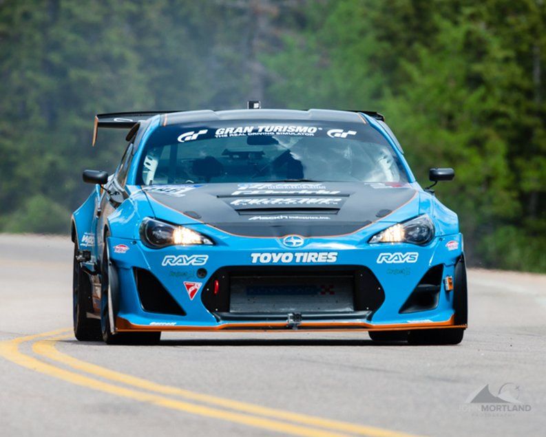 Blue race car on a winding mountain road, racing towards the viewer.