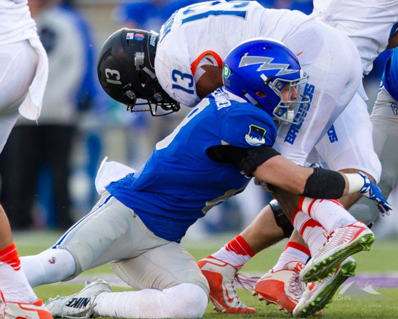Football players in blue and black uniforms colliding on a field.