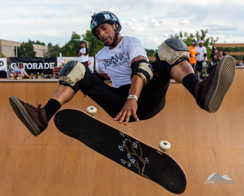 Skateboarder in mid-air above a ramp, board separating from his feet. He wears protective gear, outside a sporting event.