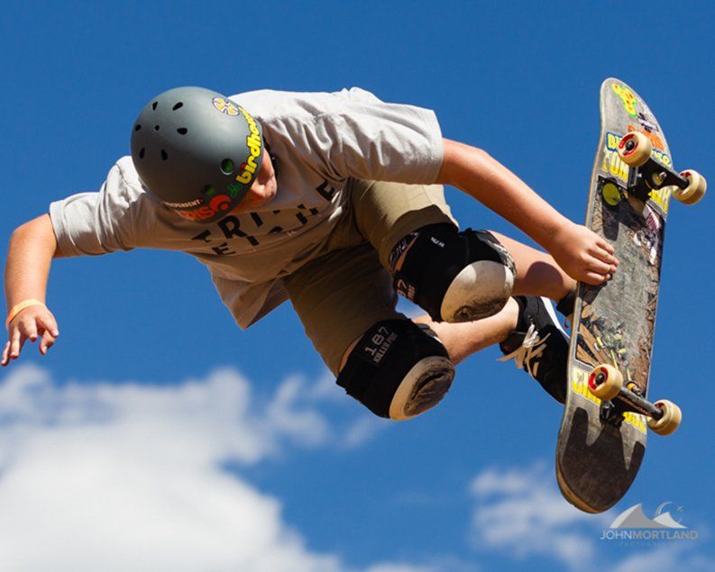 Skateboarder in mid-air, wearing a helmet and pads, against a blue sky.