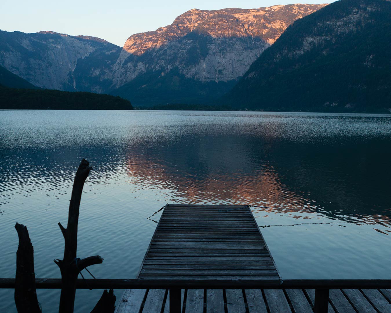 Wooden dock extends into calm lake, mountains in background at dusk.