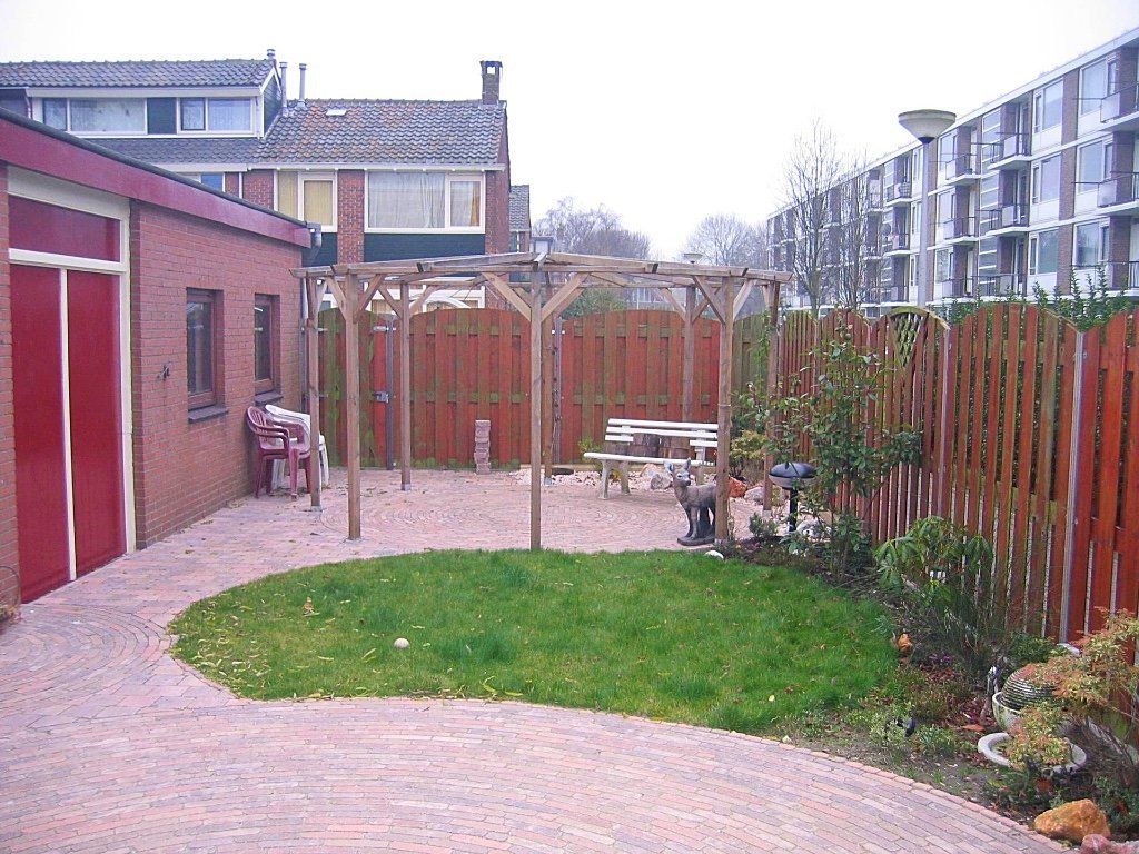 Achtertuin met een bakstenen pad, een klein gazon, een houten pergola en een houten schutting.