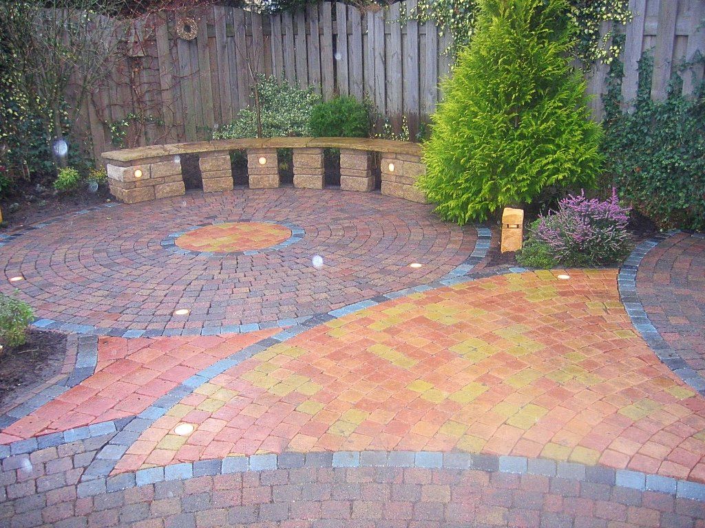 Bakstenen terras met gebogen vorm, stenen bank en aangelegde tuin.