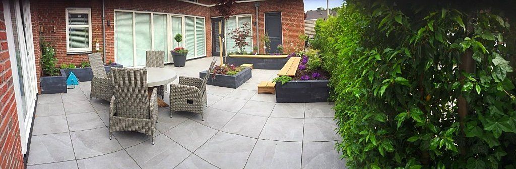 Terras met tuinmeubilair, potplanten en groene struiken.