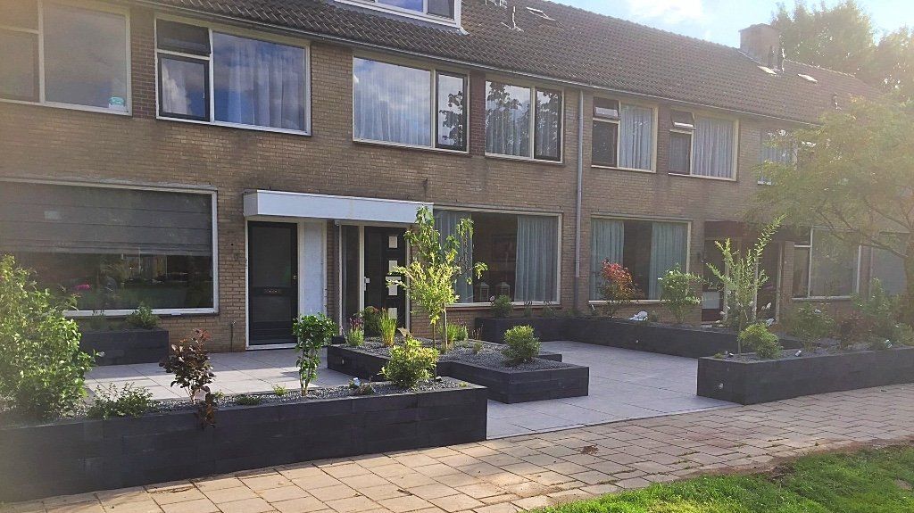 Gebouwgevel met meerdere ramen, een deur en plantenbakken ervoor. Bakstenen buitenkant, bewolkte lucht.