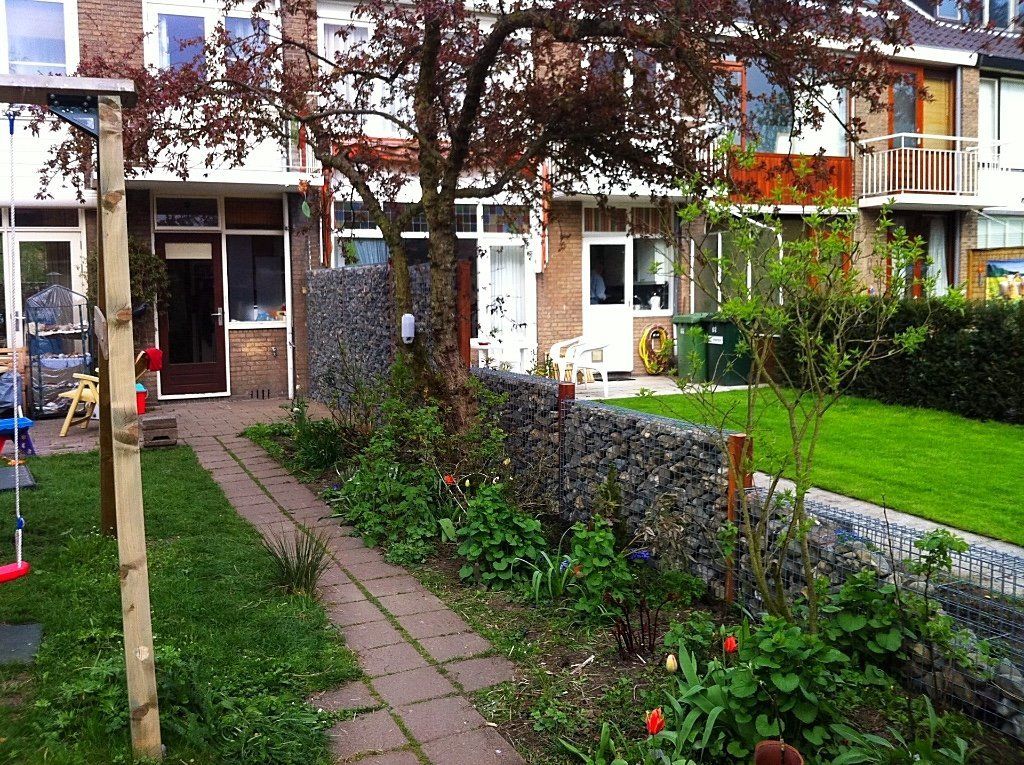 Rijtjeshuizen met stenen muren en een met bloemen omzoomd wandelpad.