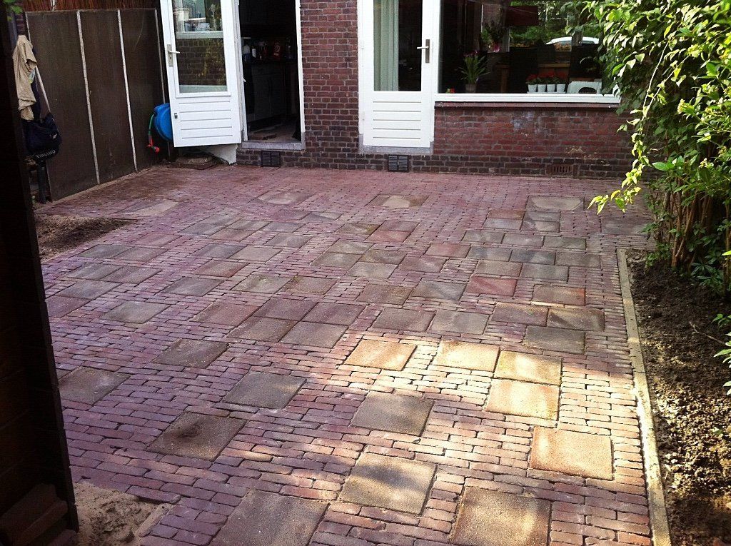 Een stenen terras buiten een stenen gebouw met witte deuren, omgeven door groen.