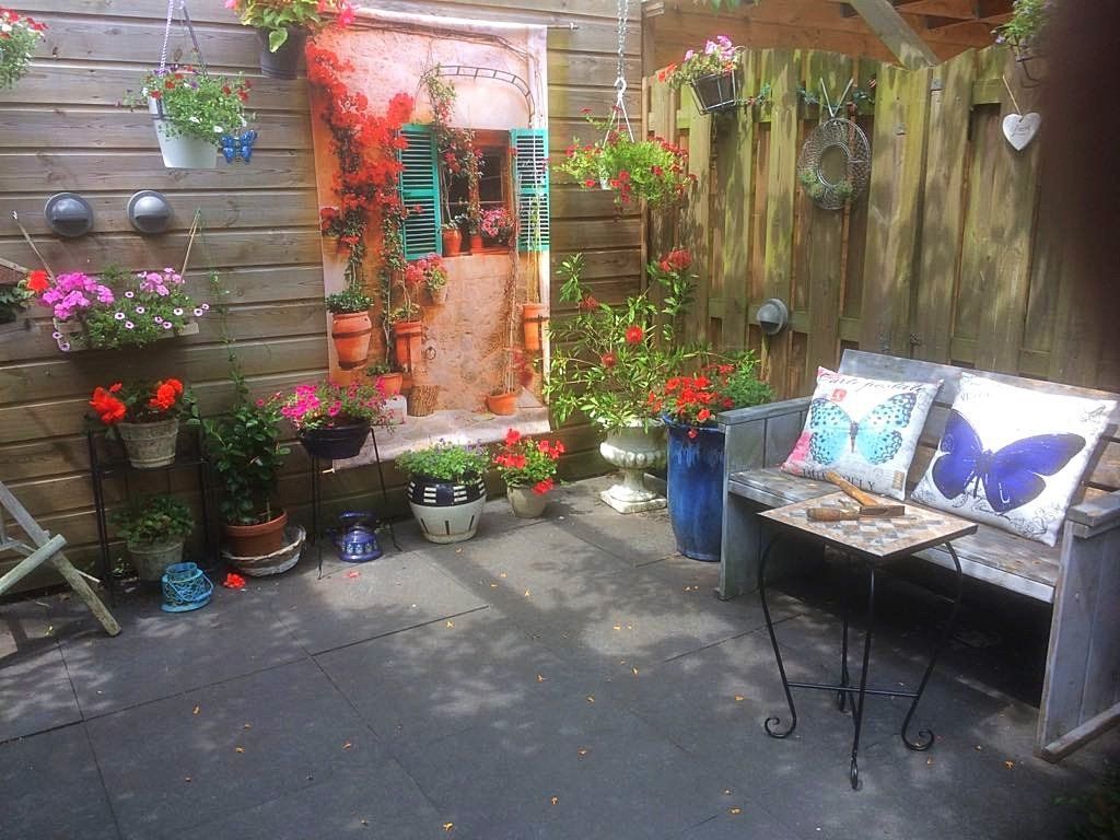 Gezellig terras met planten, een bankje met kussens in de vorm van vlinders en een decoratieve muurschildering op de deur.