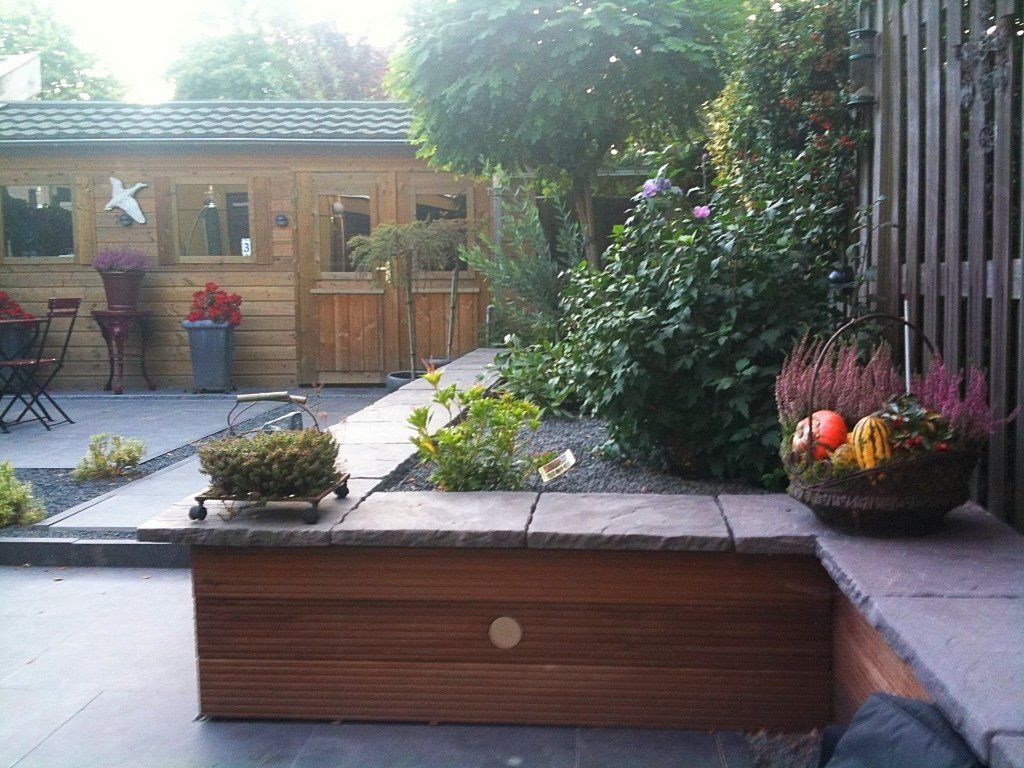 Houten tuin met schuur, bloemperken en zitgedeelte.