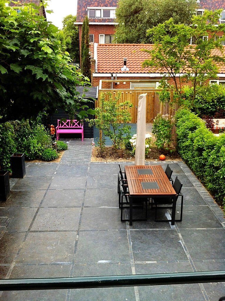 Terras met eettafel, roze bankje en groen, in een achtertuin.