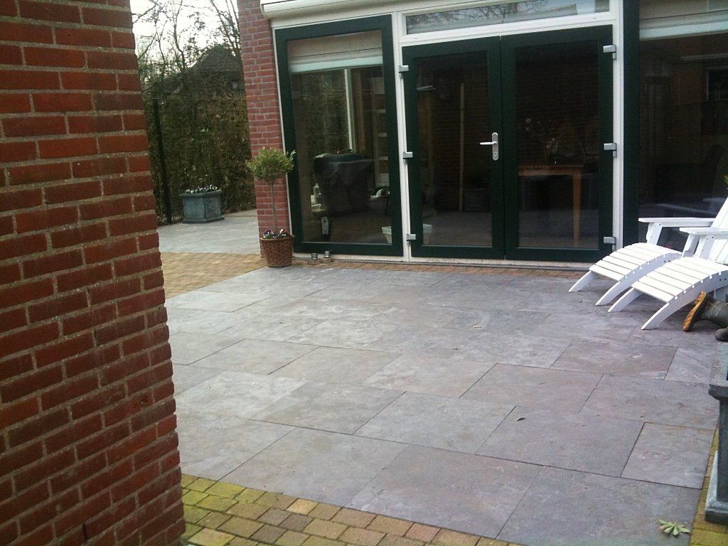 Bakstenen terras met glazen deuren, bakstenen muur en witte loungestoelen.