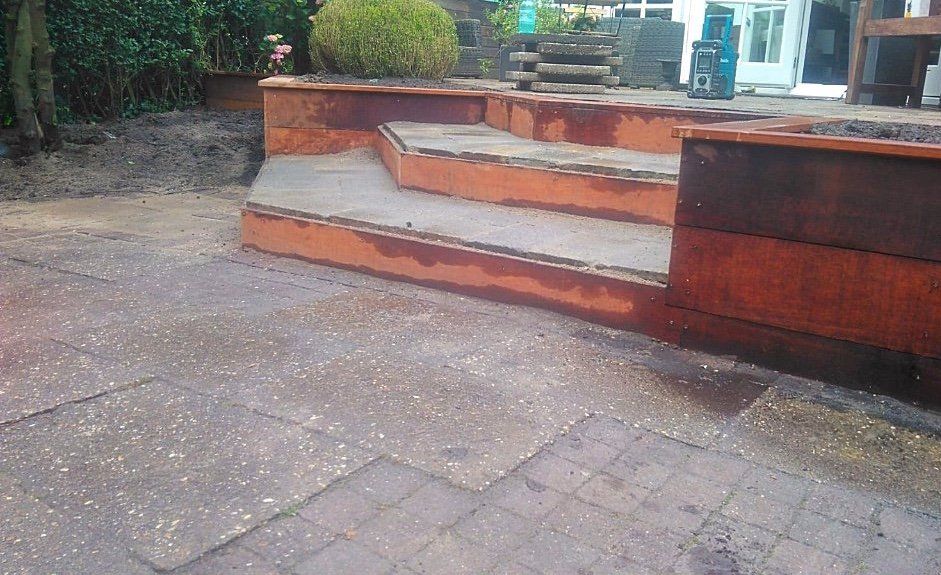 Roestkleurige metalen keermuren en trappen in een buitenomgeving met bestrating.