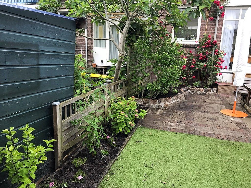 Groene tuin met houten schutting, schuur, gras en een stenen gebouw met bloemen.