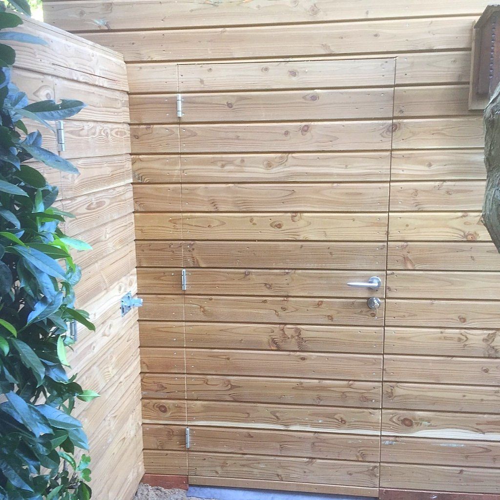 Houten muur met een deur. Groen gebladerte aan de linkerkant.