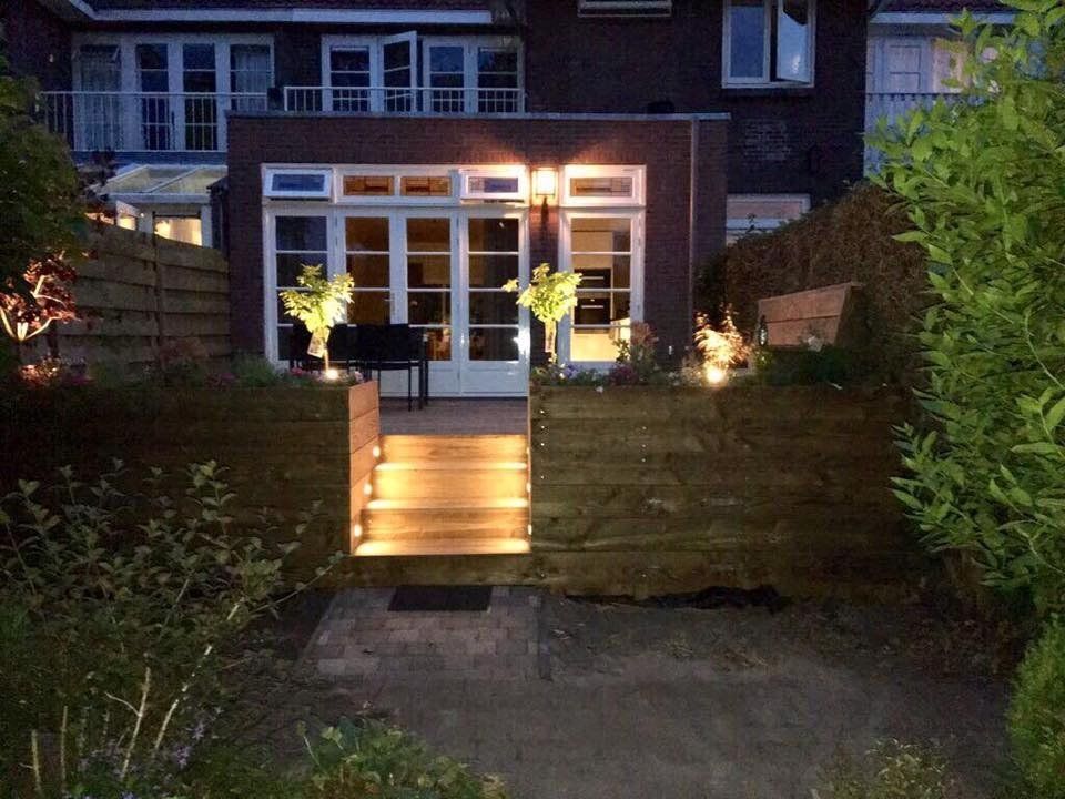 Achtertuin 's nachts met verlichte trappen die leiden naar een huis met glazen deuren en ramen, en omgeven door groen.