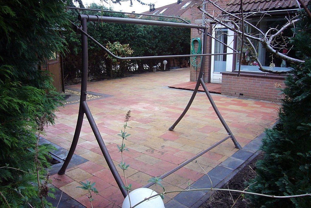 Een metalen wasrek in een met bakstenen bestrate achtertuin, omringd door groene struiken.