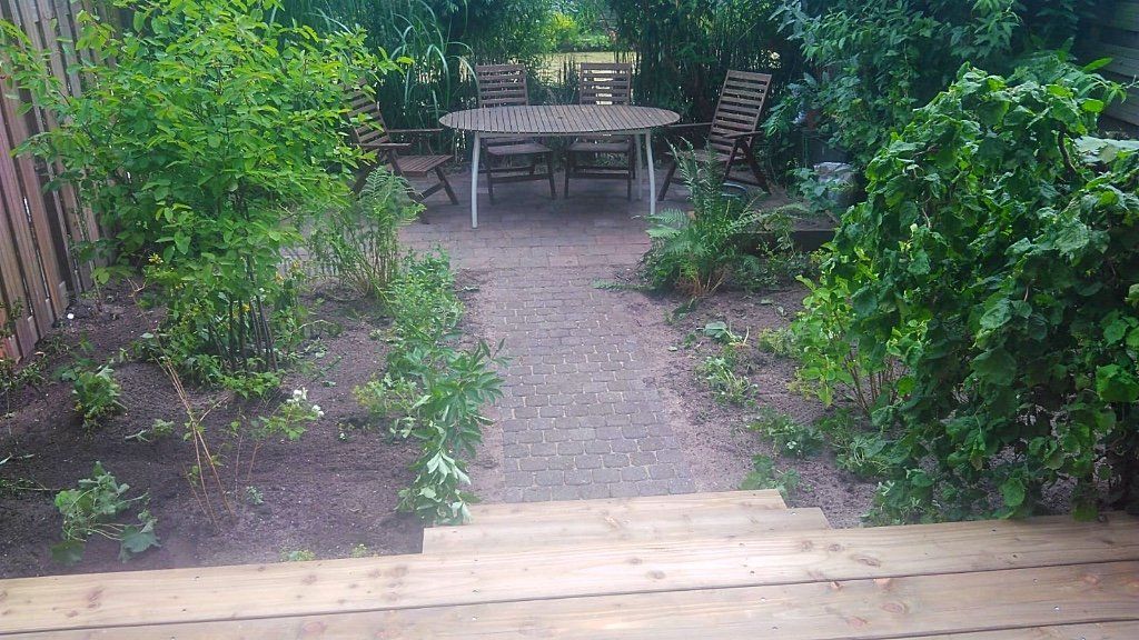 Houten trappen leiden naar een tuinpad met een tafel en stoelen, omgeven door groen.