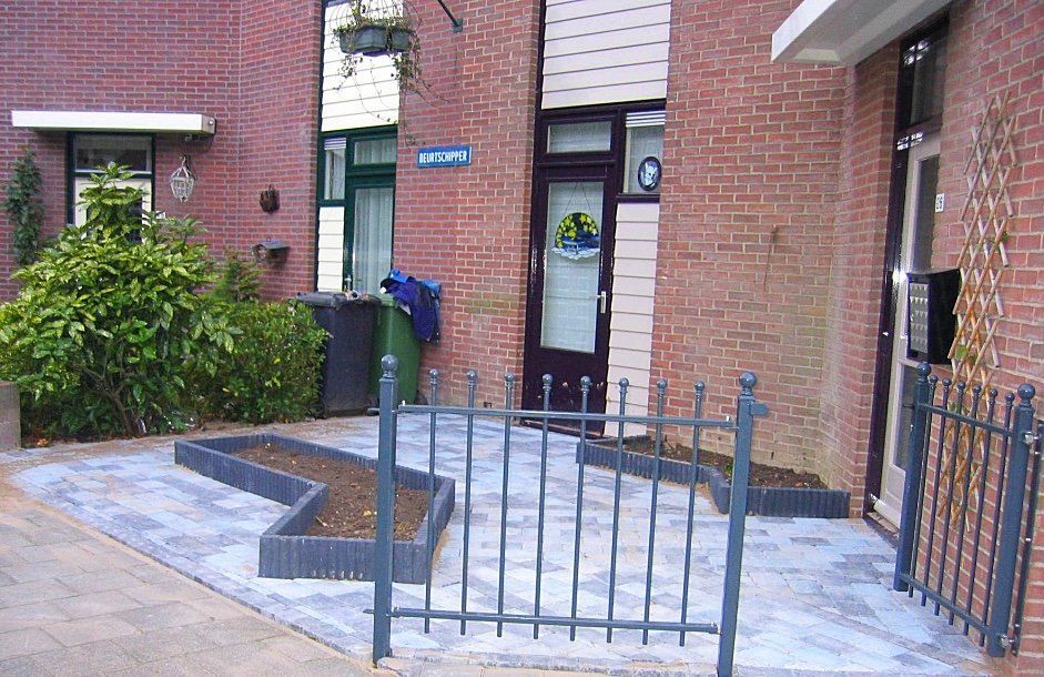 Bakstenen gebouwen met een klein omheind gebied en een zigzagvormige plantenbak op een bestrate ondergrond.