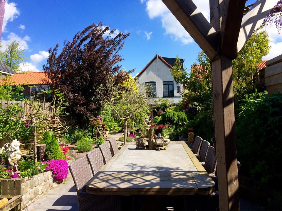 Eetgedeelte in de buitenlucht met een lange tafel, omgeven door weelderig groen en een zonnige hemel.