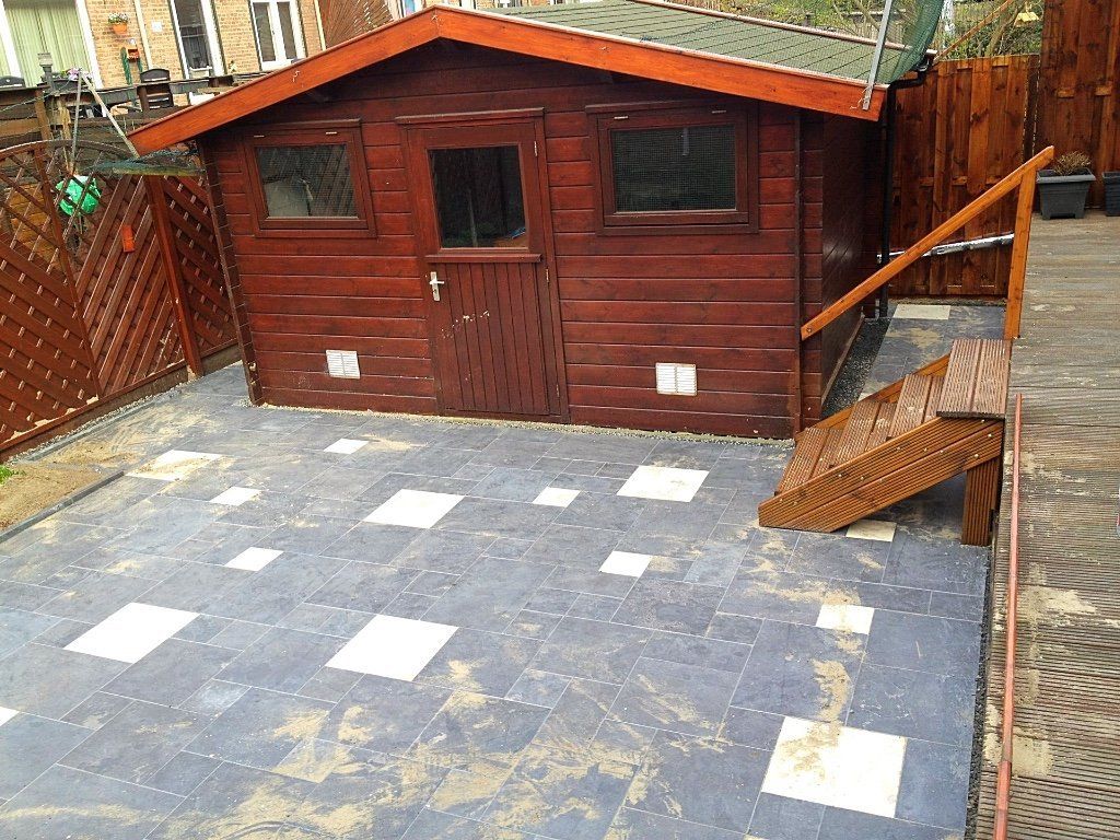 Houten schuur met trap en betegeld terras in de achtertuin. Bruine, rode en grijze kleuren.