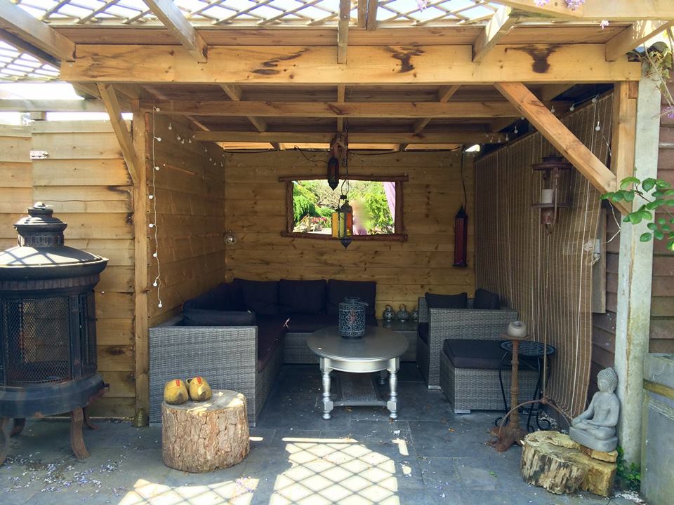 Buiten zitgedeelte met houten pergola, hoekbank, bijzettafel en decoratieve elementen.