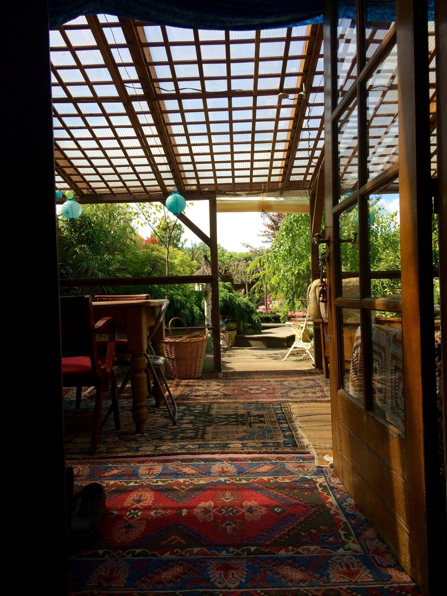 Uitzicht op een overdekt terras met een vloerkleed met patroon, een tafel en daarachter de tuin.