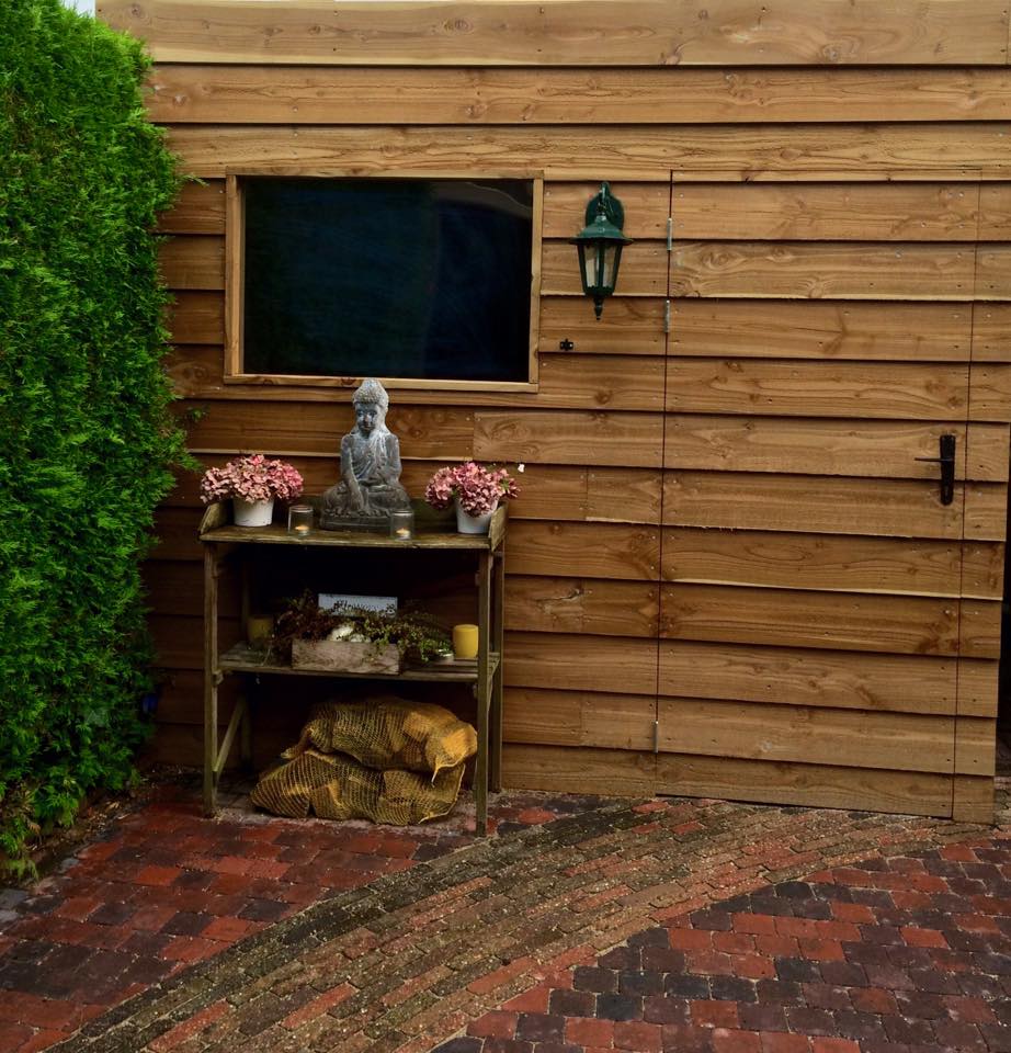 Houten schuur met een plank waarop een Boeddhabeeld staat, planten en een raam.