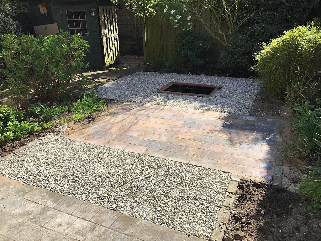 Terras met grindrand, vuurkuil en schuur in een tuinachtige omgeving.